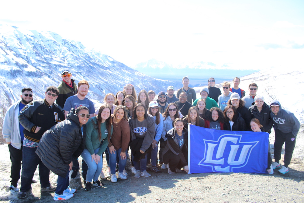 students posing with an LCU flag on a snowy mountainside