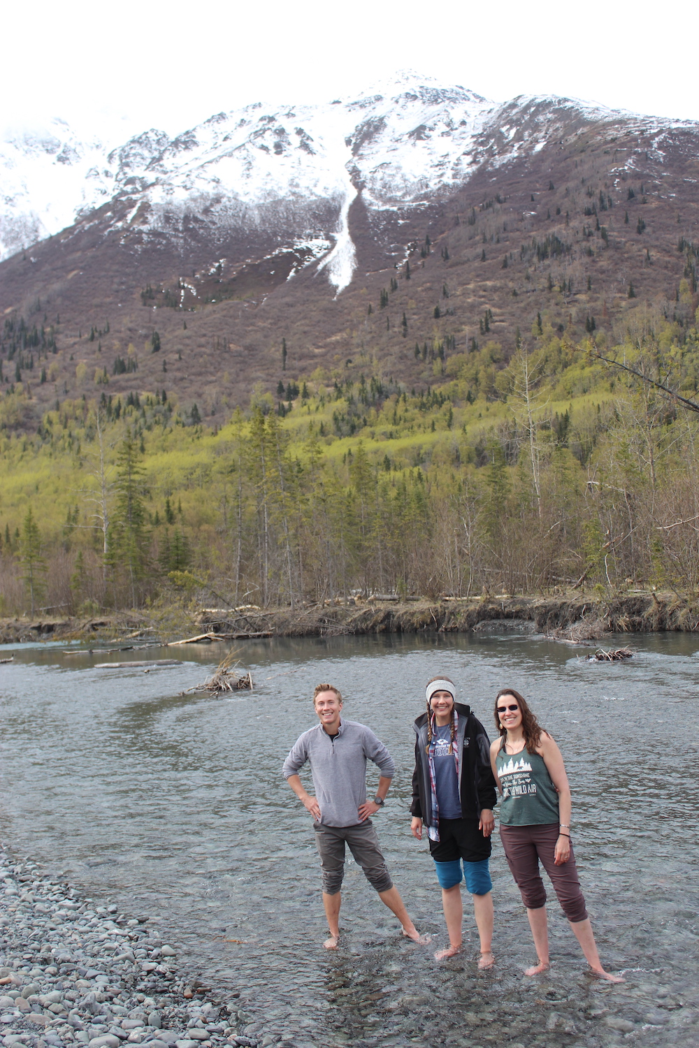 Three LCU students wading barefoot in a river at the foot of a mountain