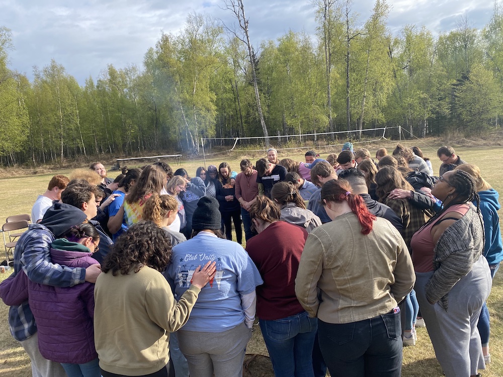 a group of LCU choir students and their hosts in Alaska circle up for a prayer