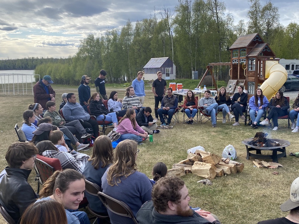 LCU choir sits around an outdoor fire for a devotional