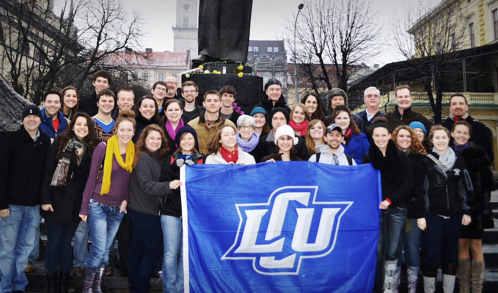 A group of choir students pose for a photo holding an LCU flag in Lviv