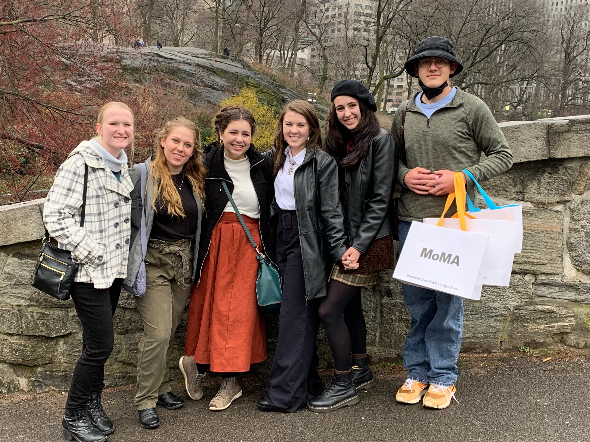 a group of students clutching shopping bags from the Museum of Modern Art smile for a photo in front of Central Park