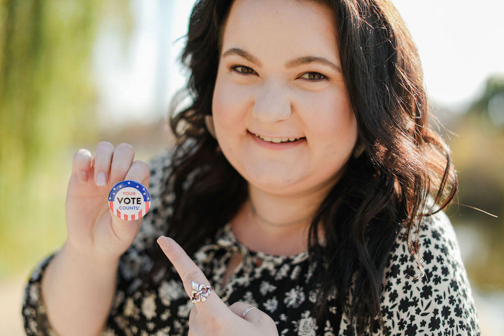 Emma holding a pin that reads, "Your Vote Counts!"