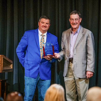 Dr. Andy Laughlin presenting Michael Mimms with his award on stage, next to a podium.