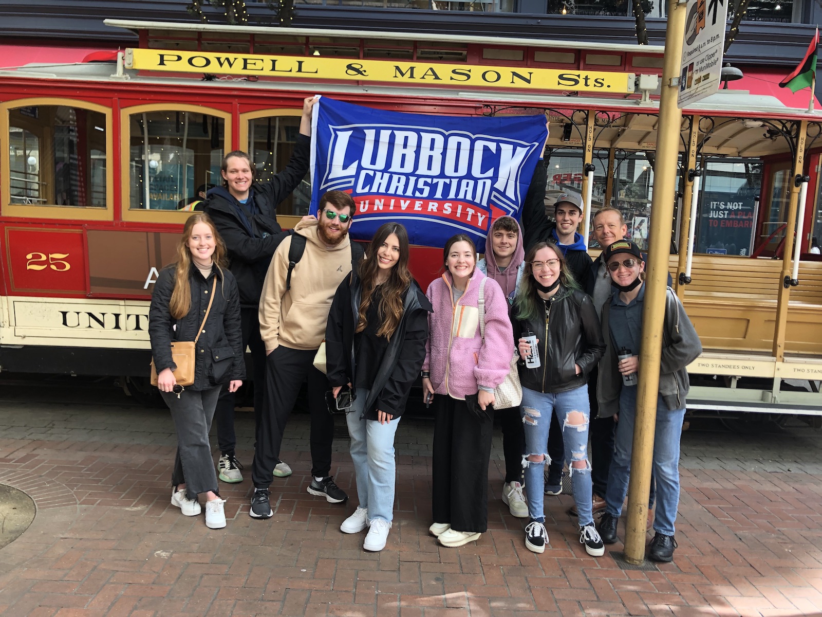 Class of students holding up an LCU flag in front of a San Francisco Cable Car