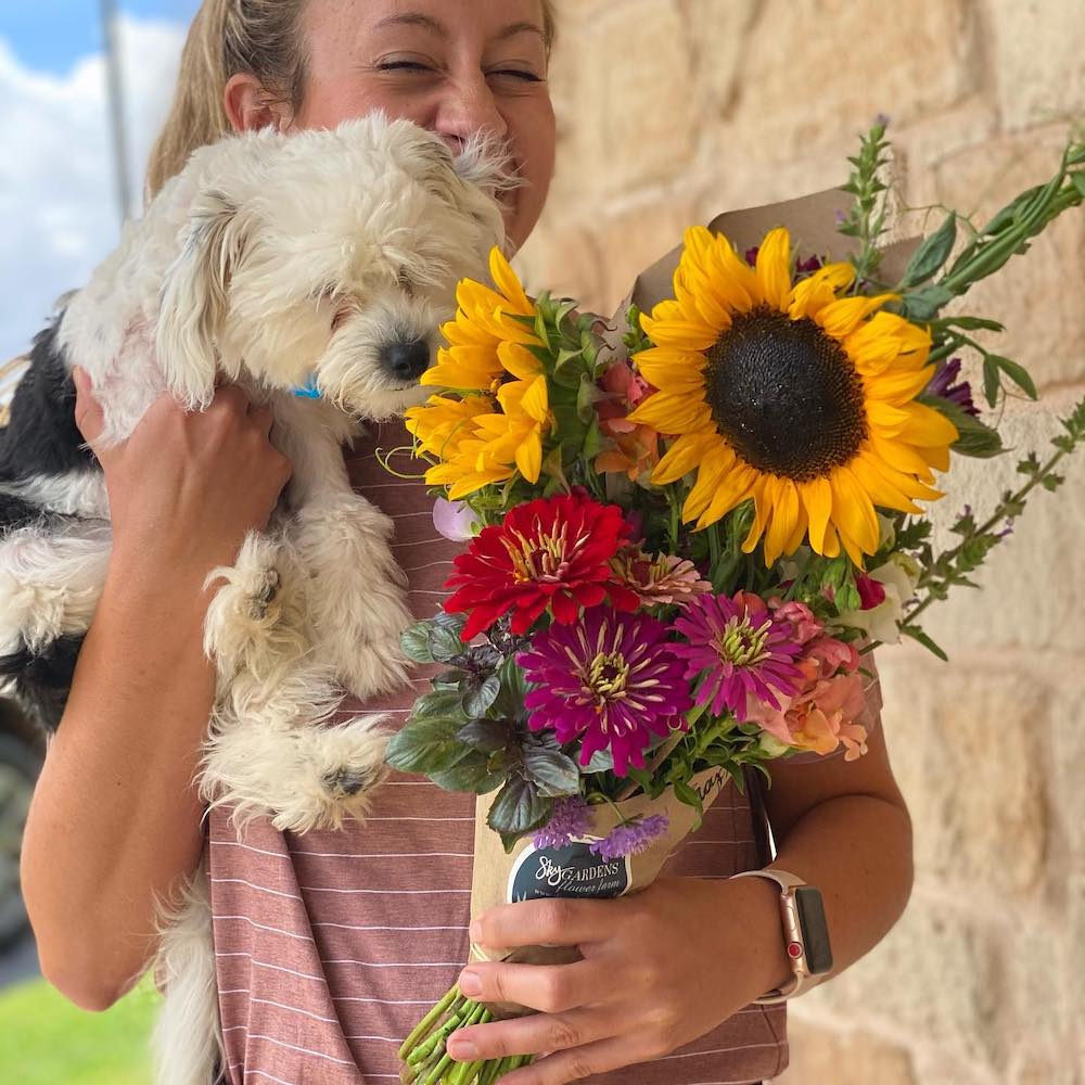 Skyler holds an arrangement of flowers in one hand and a small dog in the other