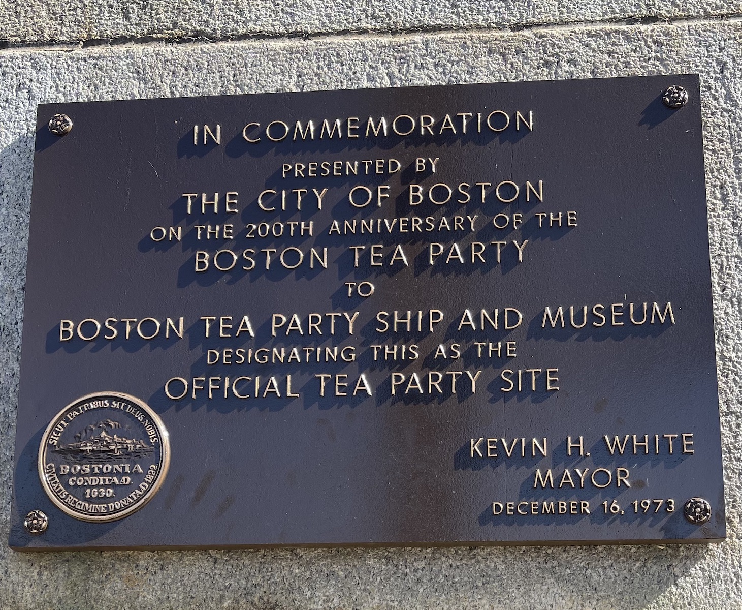 An iron plaque on a stone wall that reads: In commemoration, presented by The City of Boston on the 200th Anniversary of the Boston Tea Party to Boston Tea Party and Ship Museum, designating this as the official Tea Party site. Kevin H. White, Mayor, December 16, 1973