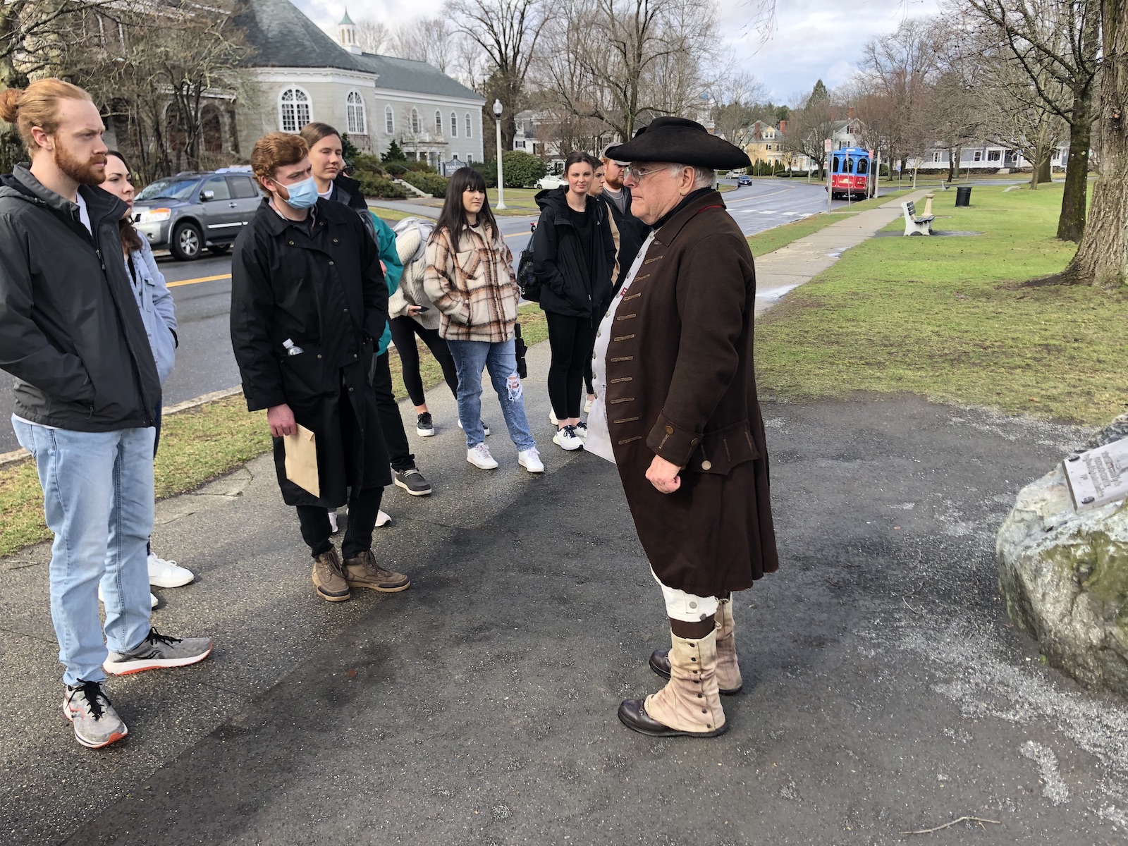 A man in colonial garb speaks to students next to a street in Lexington.