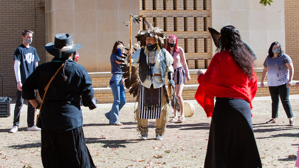 a Native American in traditional dress performs a tribal dance for LCU students