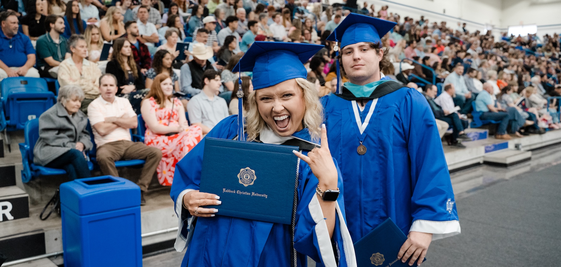 Alexis Wright giving a rock hand symbol while walking with her diploma at graduation