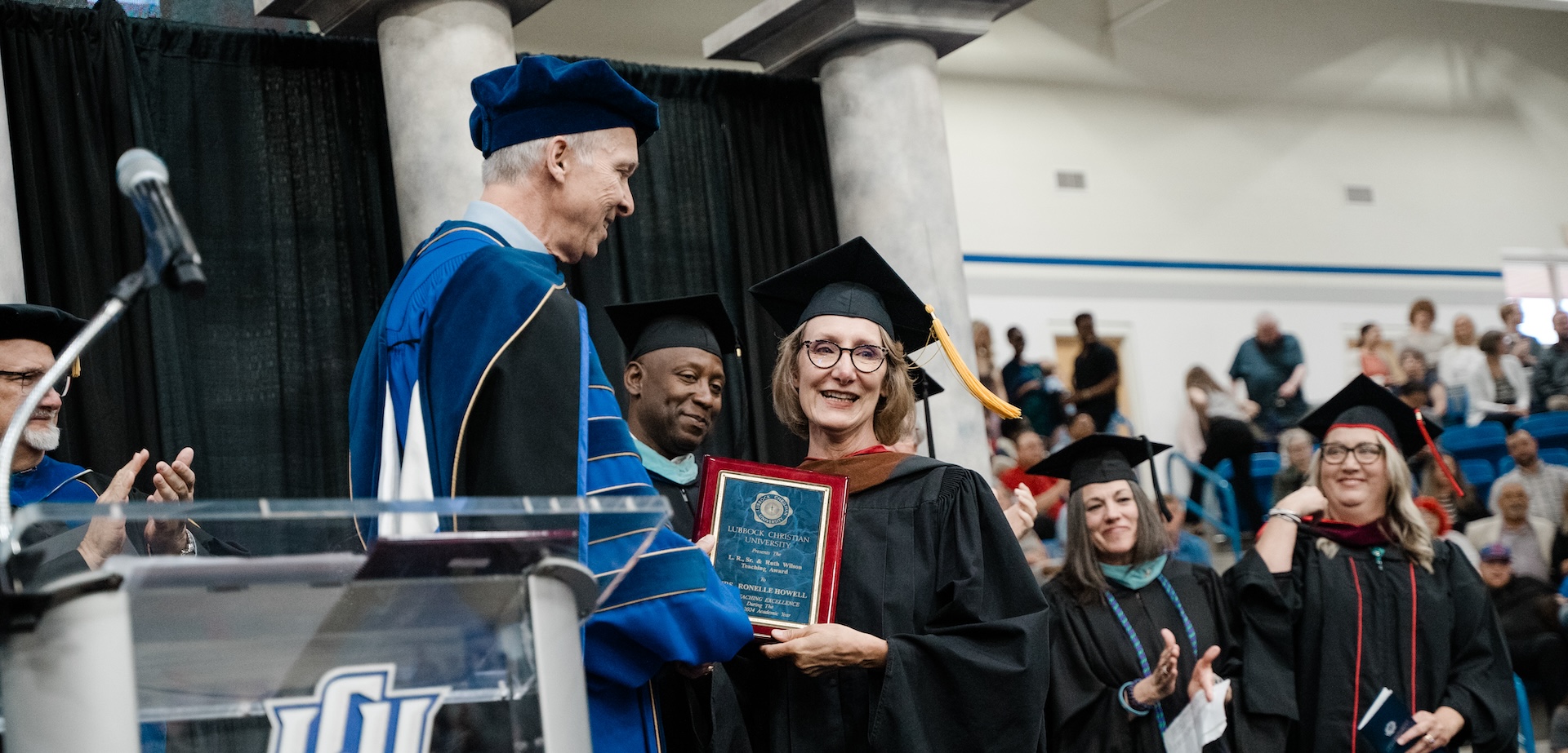 Dr. Ronelle Howell receiving a plaque on stage from President McDowell at graduation