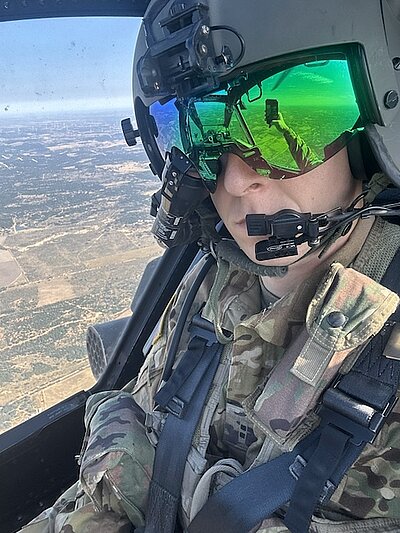 Caleb flying in the cockpit with a helmet on and ground below out the window