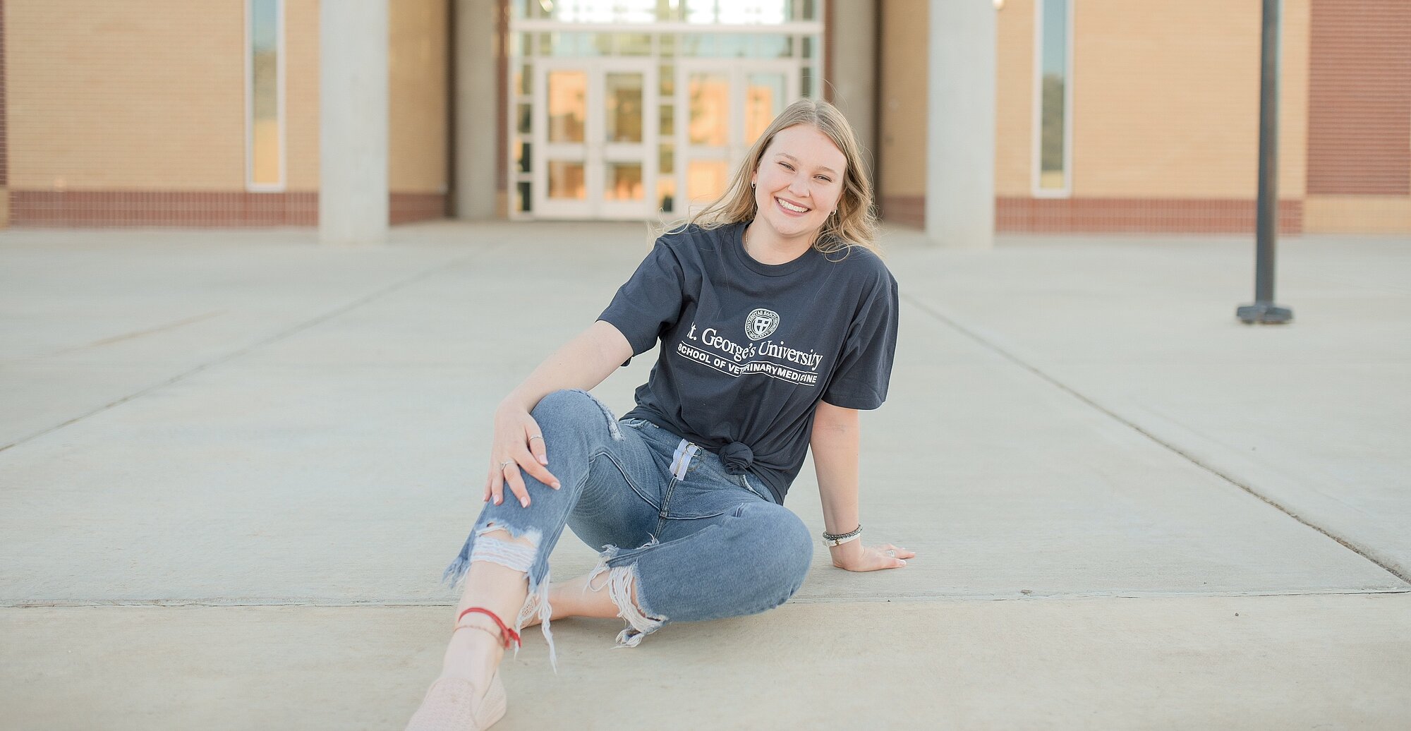 a student wearing a St. George’s University shirt sits on the ground in front of the LCU science building