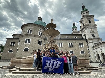 Group of LCU Students holding an LCU flag in front a church looking building
