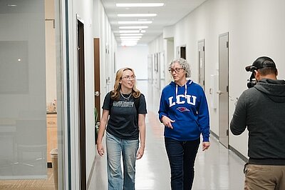 Video crew capturing Lily walking with a professor down a science hallway