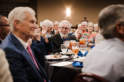 Don sitting at his table at the dinner smiling after a comment from the stage