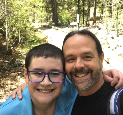 Michael posing for a picture with his son on a hike in the woods