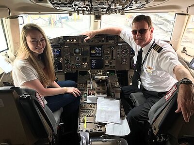 Jade in the cockpit of an airline with dad in uniform in the Copilots seat.