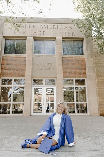 Alexis' senior pictures posing in cap and gown in front of the American Heritage Building at LCU