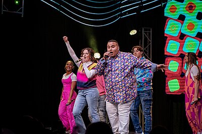 hosts and hostesses from the most recent show performing on stage in colorful costumes