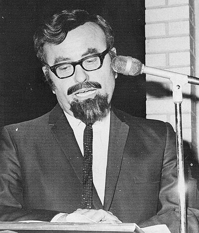 Dr. Harvey Pruitt wearing a disguise in front of a microphone