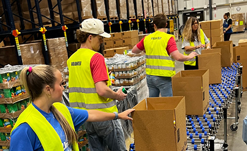 4 students loading boxes on a conveyor belt for a food bank