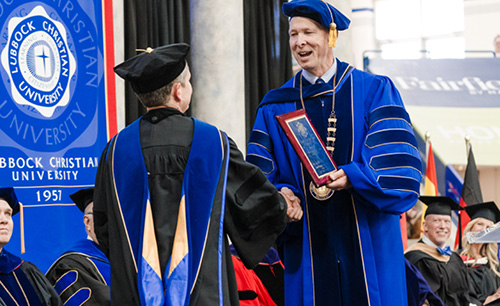 Dr. Laci Richardson receiving a plaque from President McDowell on stage at graduation