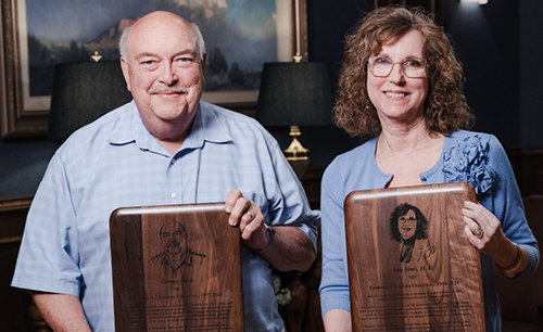 Two retirees posing with their retirement plaques