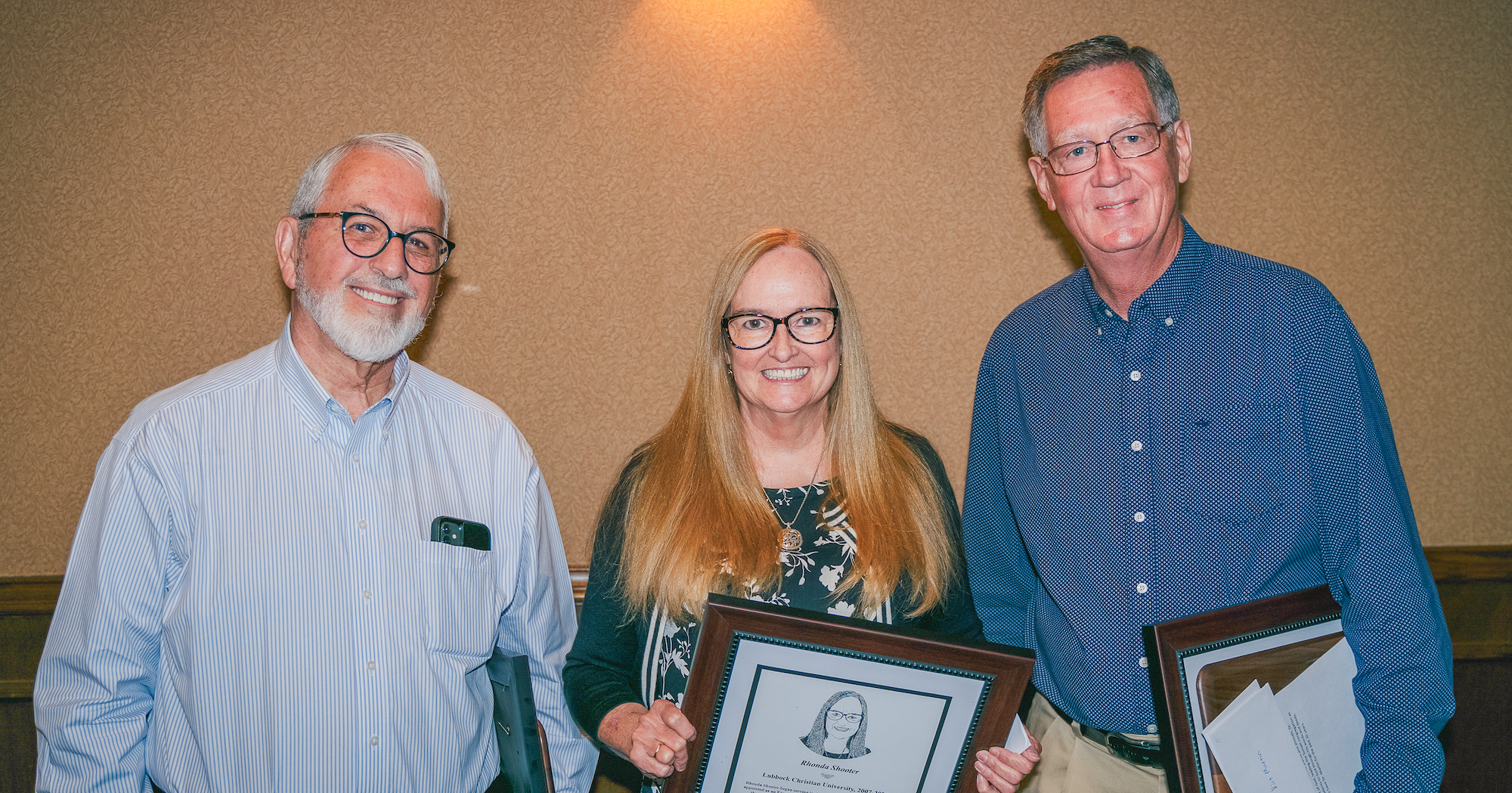 Three retirees smile for a photo holding recognition plaques. 