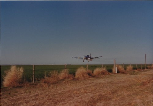a plane flying close to the ground over a crop field