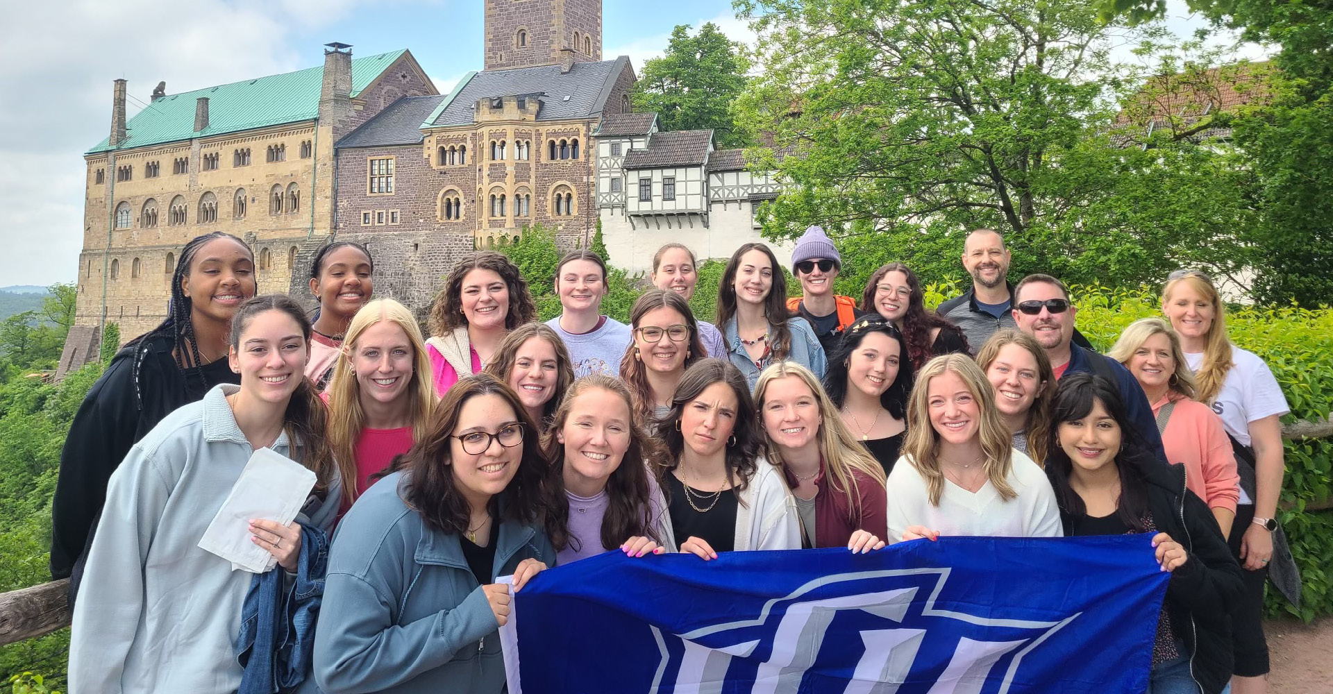 Students on a trip in front of an iconic building holding a LCU flag