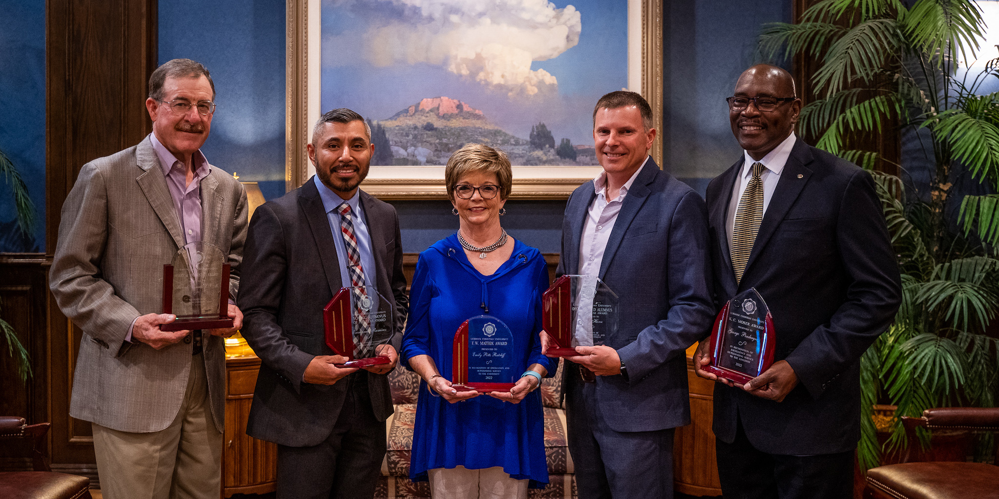 Five people holding awards pose for a photo in front of a painting