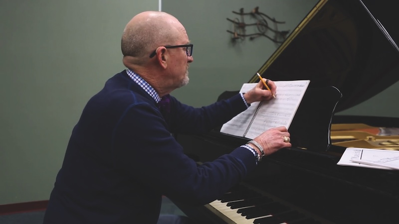 Photograph of Dr. Rogers sitting at a piano writing on a piece of music