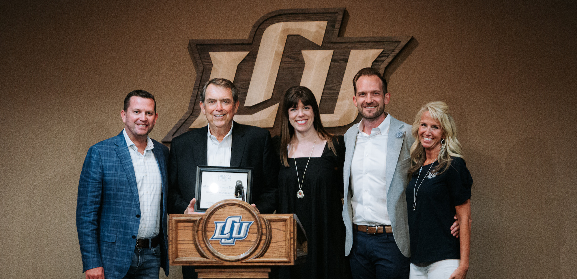 Five people smile for a photo behind a podium holding an award plaque.