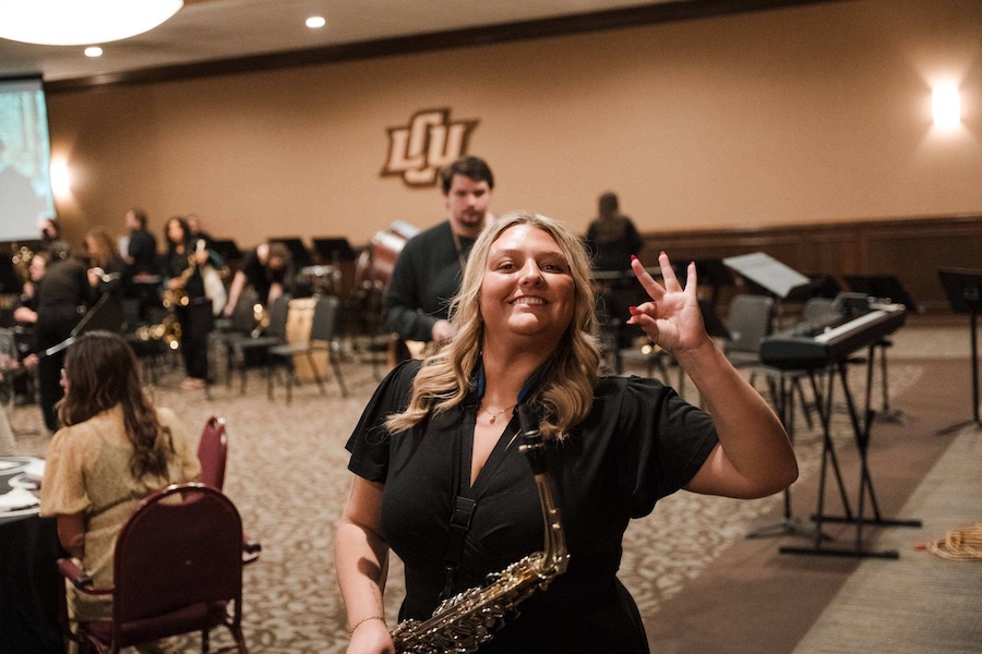 Portrait of Molly Davidson holding her instrument with the other hand doing the chap hand sign.