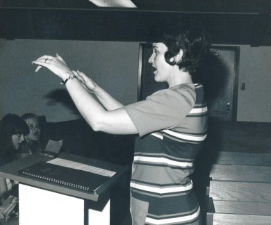 black and white photo of a young Peggy West conducting a choir