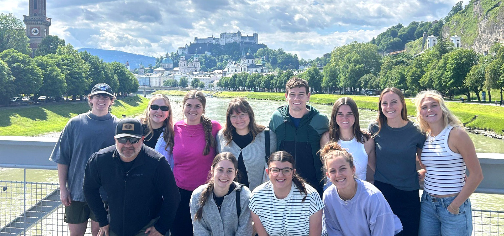 group of students posing before a landscape of a river and mountain with castle on top