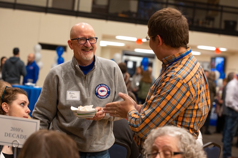 Photograph of Dr. Rogers smiling and talking with an alumnus at a luncheon