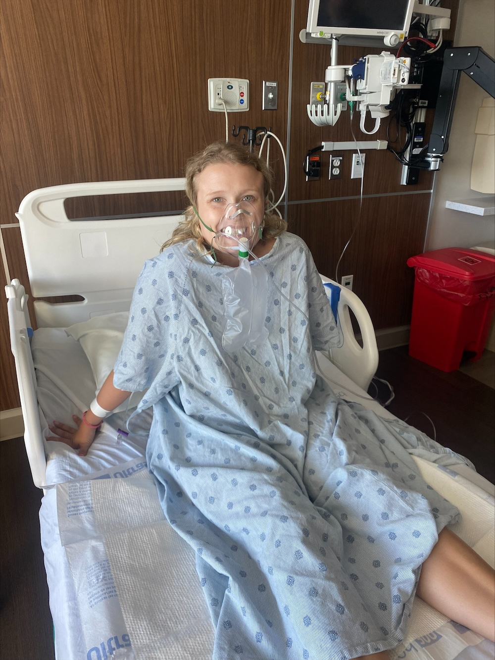 Alexis with respirator mask on in a hospital bed